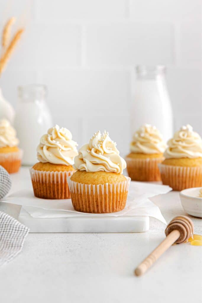 Five honey cupcakes topped with swirls of honey buttercream frosting.