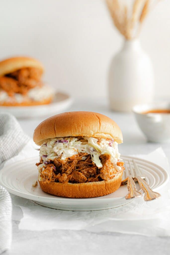 Pulled pork sliders with coleslaw served on appetizer plates with small forks.