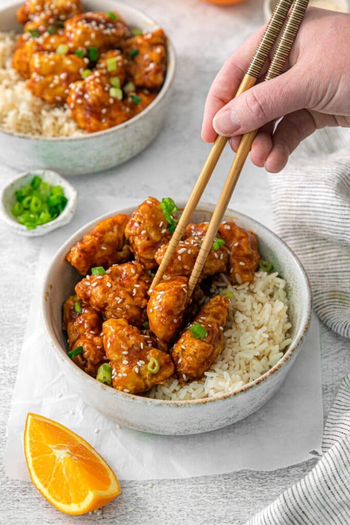 Air fryer orange chicken being lifted from a bowl with chopsticks.