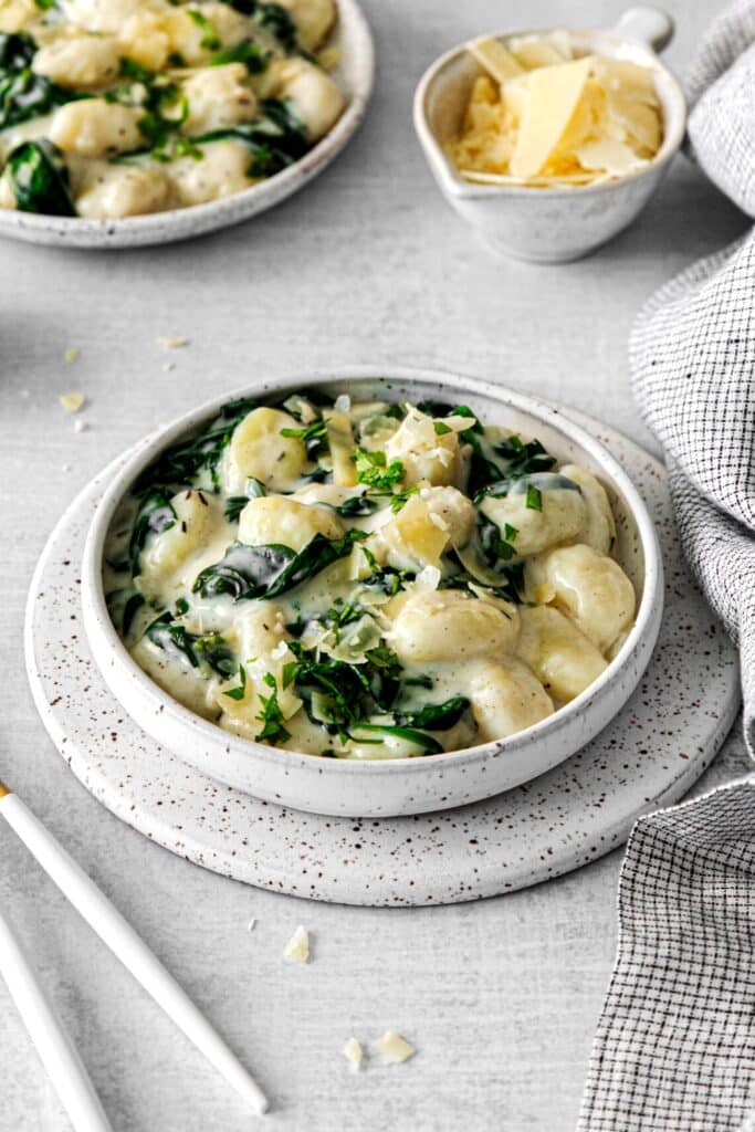 Creamy parmesan spinach gnocchi on a dinner table with a small dish of shaved parmesan.
