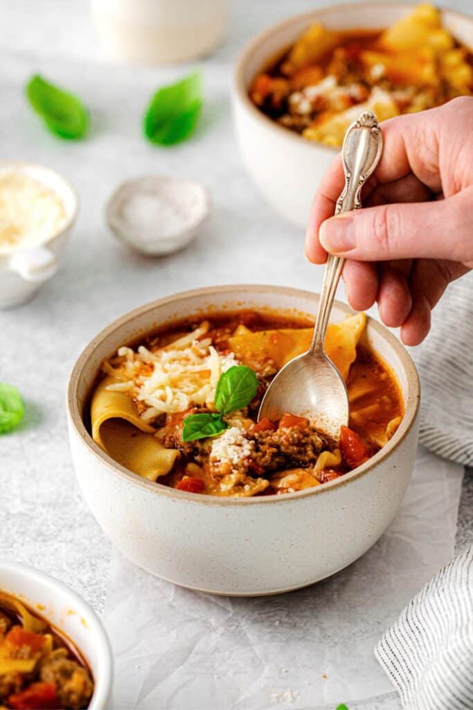 A bowl of lasagna soup on a dinner table with spoon.