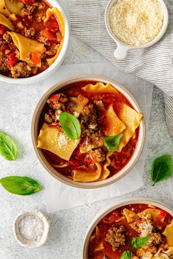 A serving of lasagna soup garnished with grated parmesan and fresh basil leaves.