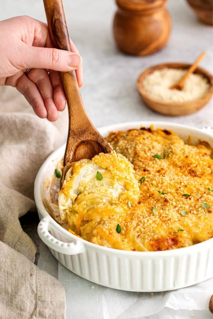 Potatoes au gratin with gruyere being scooped and served with a wooden spoon.