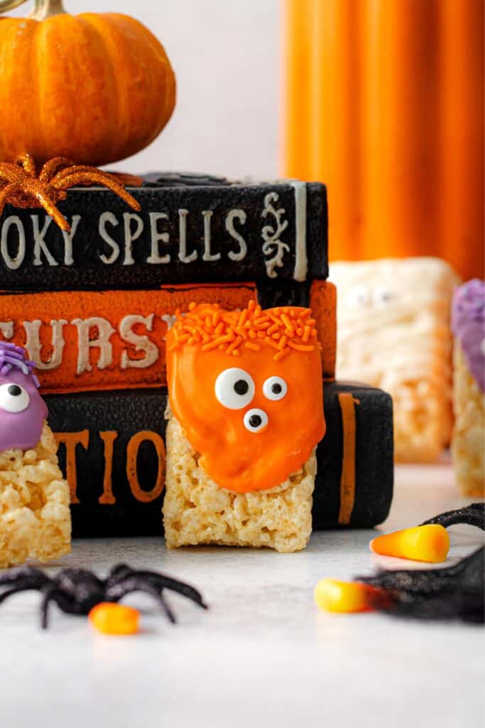 An orange Monster Rice Krispie treat leaning against a stack of witches spell books.