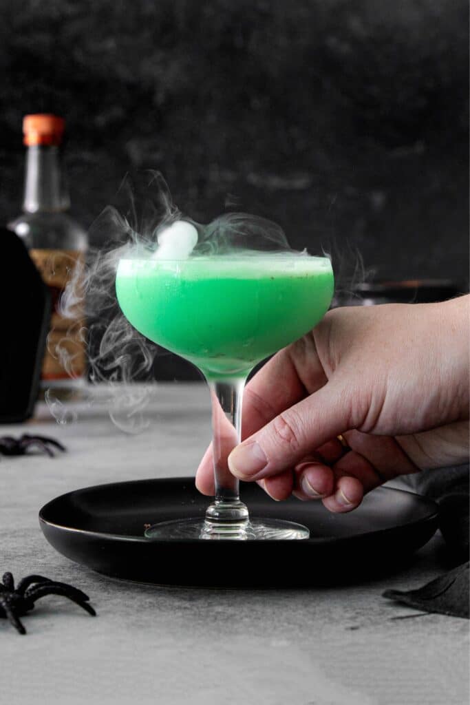 A hand lifting a cocktail glass off of a Halloween table. It's a mint martini.