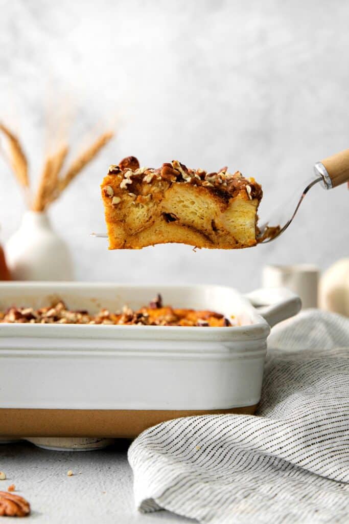 A slice of pumpkin bread pudding being lifted with a spatula from a baking dish.