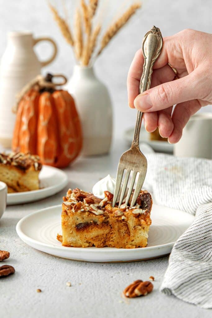 A fork in hand digging into a square of pumpkin bread pudding.