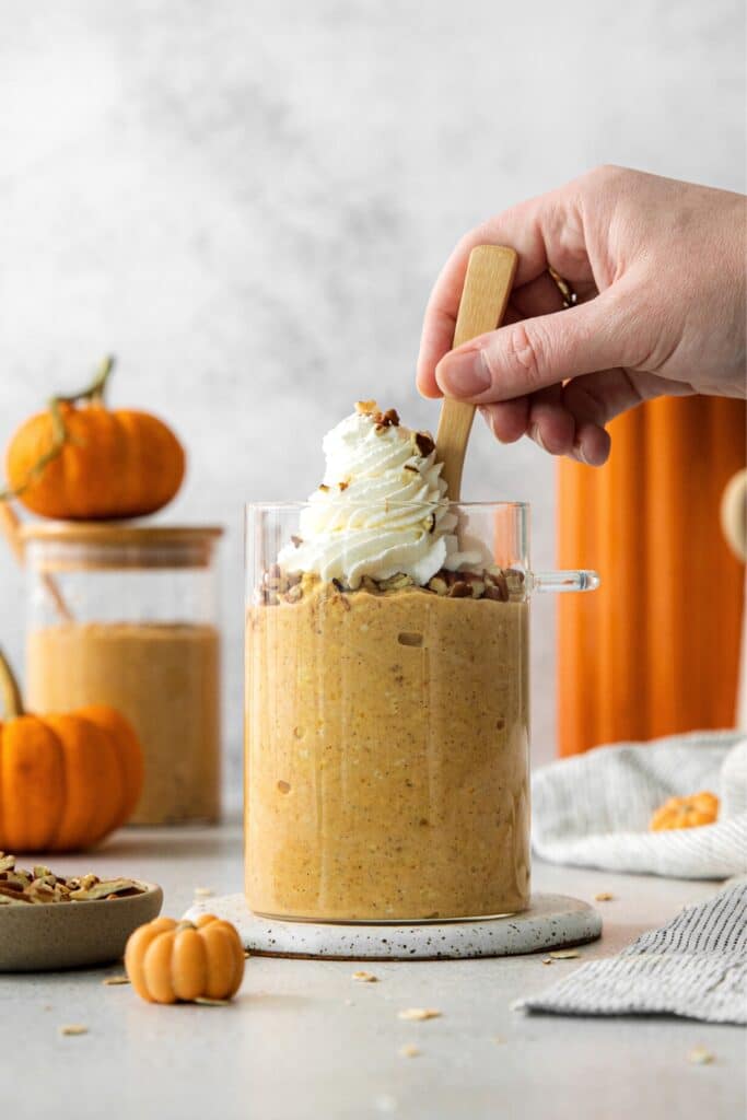 Pumpkin overnight oats in a glass jar with pecans, whipped cream and a spoon.