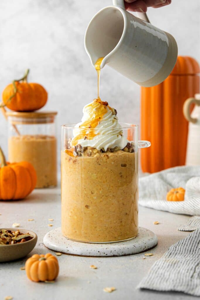 Pumpkin pie overnight oats served for breakfast in a glass cup with chopped pecans and whipped cream.