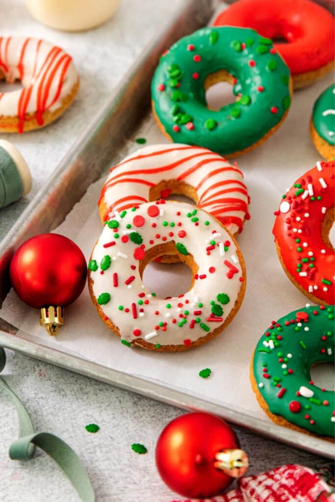 Christmas donuts, glazed and decorated with holiday sprinkles, on a baking tray.