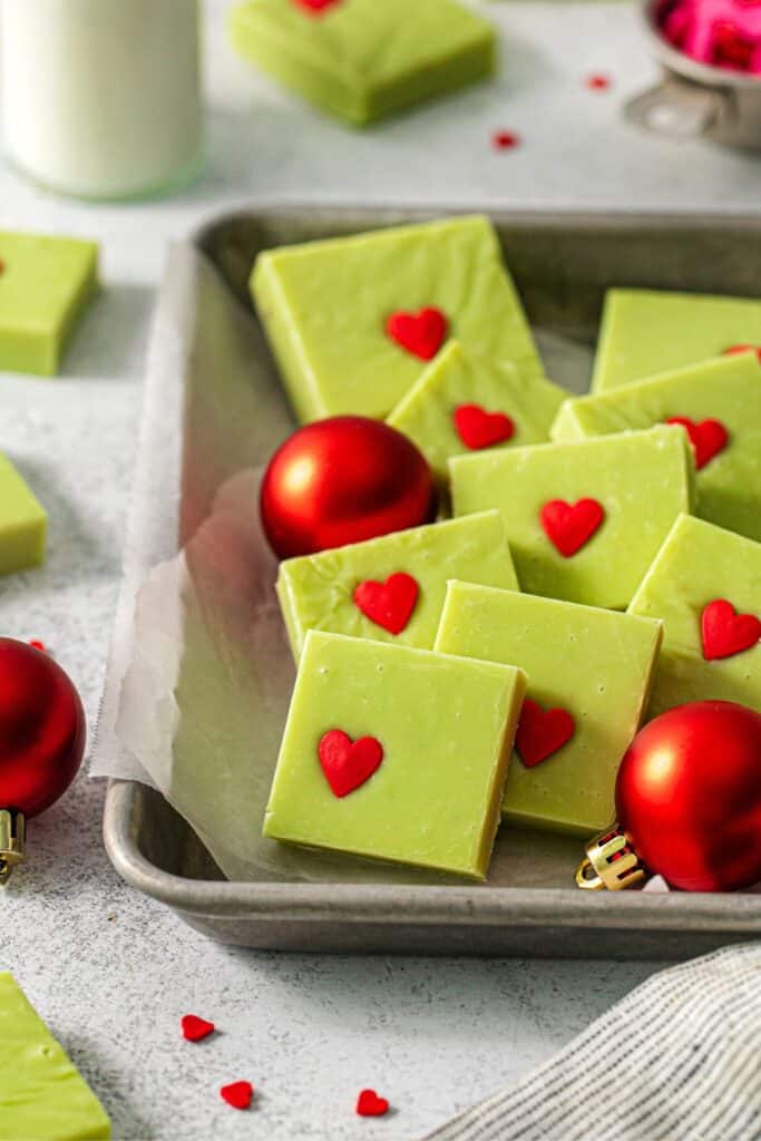 Squares of Grinch fudge arranged on a tray with red Christmas bulbs.