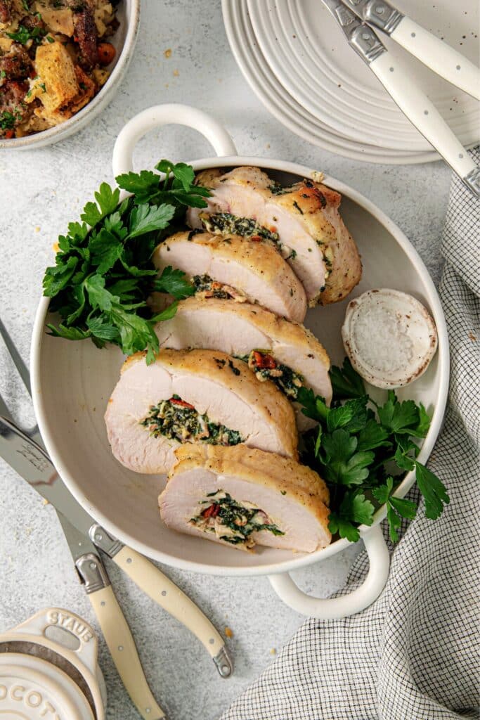 Thick slices of stuffed turkey breast filled with spinach, ricotta and bacon, in a white serving dish.