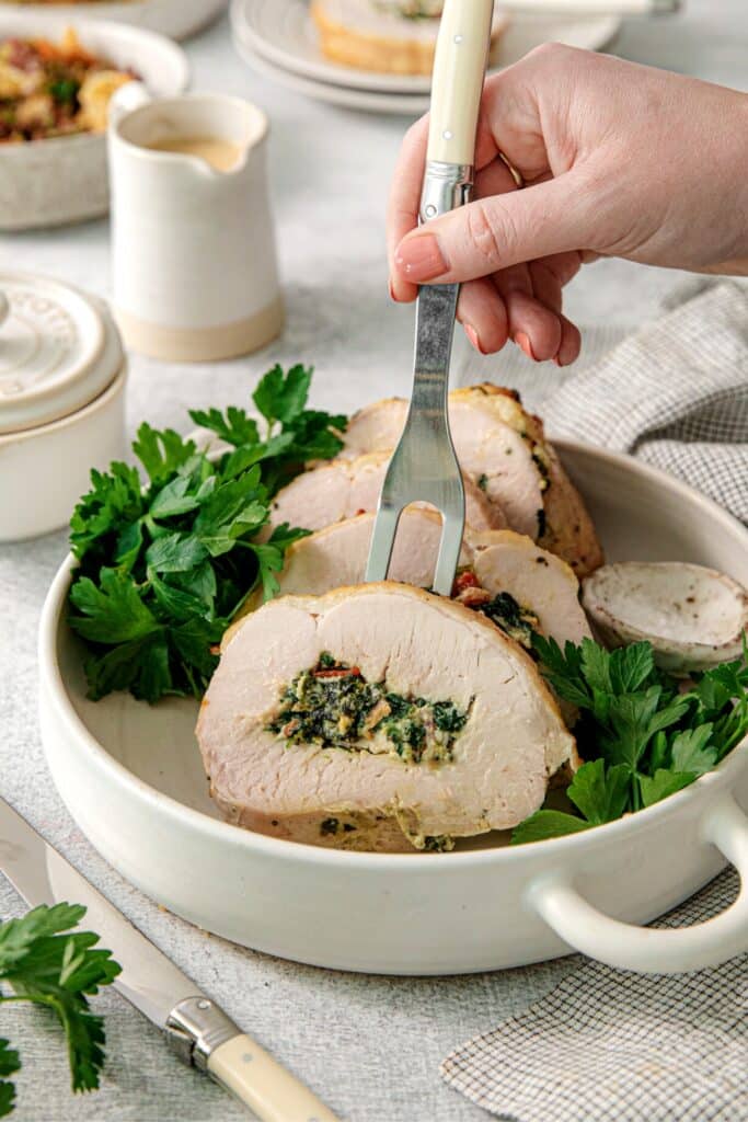 A serving fork lifting a slice of stuffed turkey breast from a serving dish.