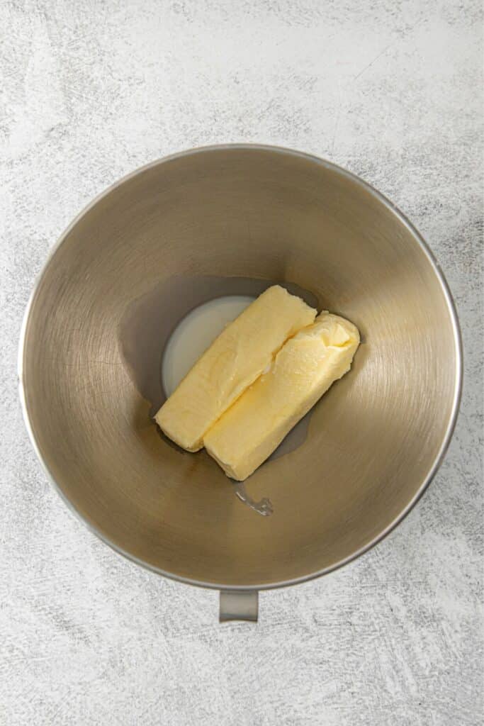 Two sticks of softened butter with a splash of whole milk in the metal bowl of a stand mixer.