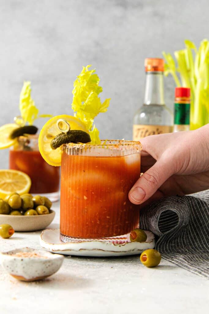 A hand reaching for a Bloody Mary cocktail.