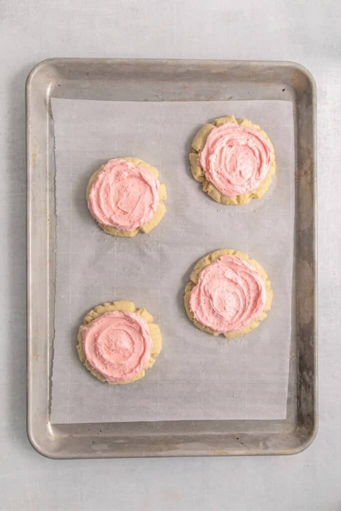 Frosted pink sugar cookies with a sprinkling of white sparkling sugar on a baking tray.