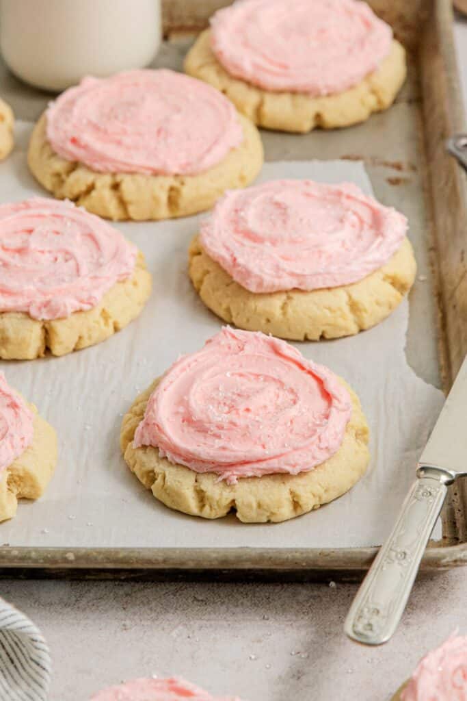 A batch of (copycat) Crumbl pink sugar cookies on a lined baking tray.