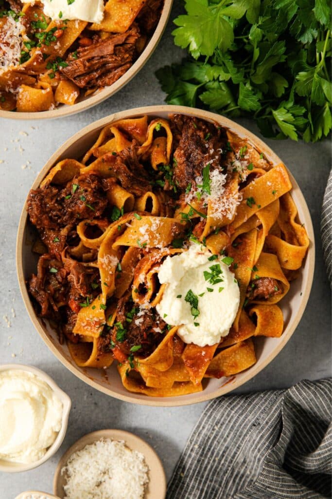 A serving of short Rib Ragu with pappardelle and a dollop of ricotta cheese.