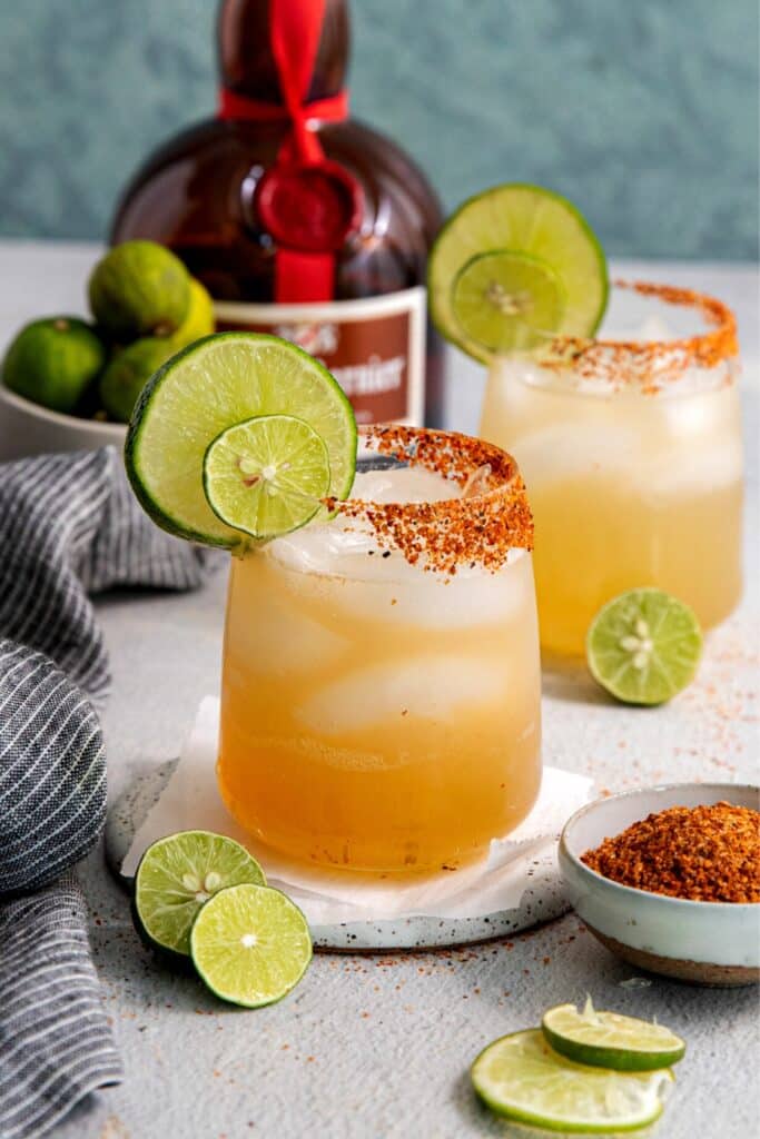 A top-shelf Cadillac Margarita in a cocktail glass rimmed with Tajin and garnished with lime wheels.